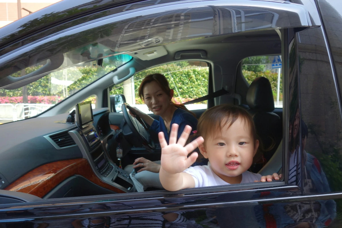 Anak melambai dari jendela mobil; foto stok